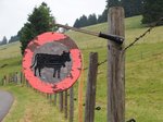 Das Bild zeigt einen Weidezaun. Daran hängt ein stilisiertes "Zufahrt Verboten"-Schild mit einer Kuh in der Mitte.