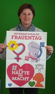 Das Bild zeigt MdL Rosi Steinberger mit einem Plakat zum Weltfrauentag. Darauf steht neben einigen Symbolen "Internationaler Frauentag - Die Hälfte der Macht".
